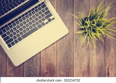 Working Table With Laptop Computer And Plant Pot. Wooden Table Background With Copy Space On Bottom. Instant Photo Vintage Split Toning Color Effect.