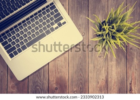 Working table with laptop computer and plant pot. Wooden table background with copy space on bottom. Instant photo vintage split toning color effect.