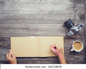 Working table with notebook paper, coffee cup , Pencil, Vintage camera , Wooden desk background with copy space on top. Soft focus with noise. Instant photo vintage split toning color effect. 