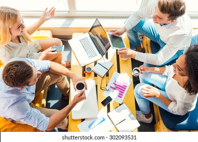 Working Together For Better Results. Top View Of Four Happy Young People Working Together While Sitting At The Wooden Desk In Office