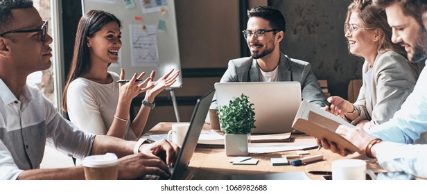 Working together. Group of young modern people in smart casual wear discussing business and smiling while sitting in the creative office