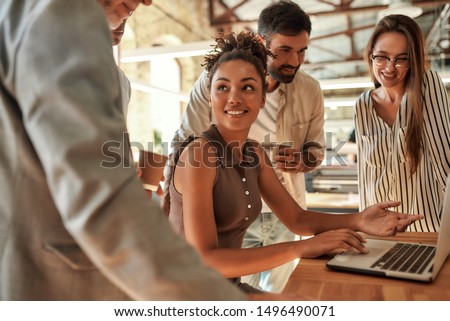 Working together. Young and cheerful afro american woman using laptop and discussing something with colleagues while sitting in the modern office. Teamwork. Office life