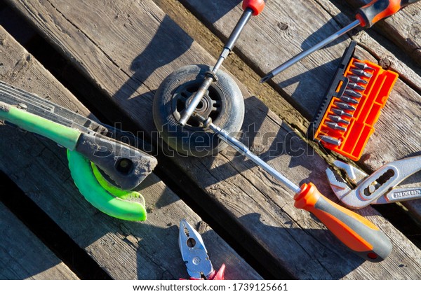 working tools are an adjustable wrench, a\
screwdriver with interchangeable bits, pliers, on wooden pallet.\
Near lies a scooter wheel. repair concept in car service and\
scooter. copy space flat\
lay.
