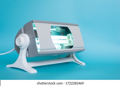 Working Ultraviolet Lamp On A Blue Background. The Concept Of Protecting And Cleaning Rooms And Objects From Bacteria And Viruses. Medicine And Healthcare.