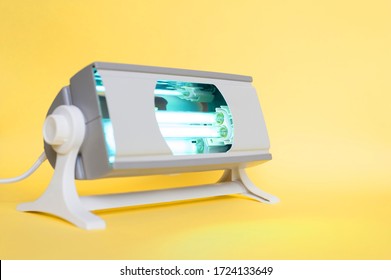 Working Ultraviolet Lamp On A Yellow Background. The Concept Of Protecting And Cleaning Rooms And Objects From Bacteria And Viruses. Medicine And Healthcare.
