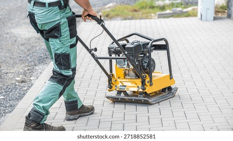 Working with vibro-compaction plate to compact self-locking blocks in their laying bed. Vibrating plate in construction.