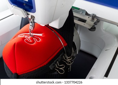 Working White Embroidery Machine Embroidering Logo On Red And Black Sport Cap, Close Up Picture