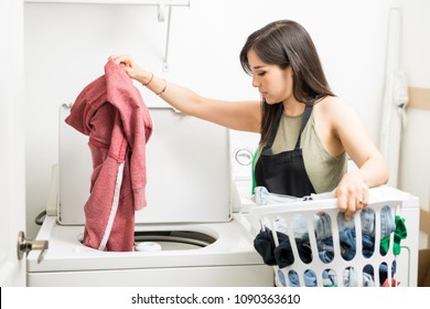 Working Woman Adding Clothes To Machine For A Wash Holding White Laundry Basket