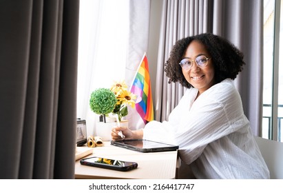 Working woman LGBTQ+ Afro hair style African American lesbian, Beautiful gay working on tablet with love moment spending good time together, lgbt rainbow, pride flag on table near curtain at window.