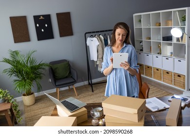 Working woman at online shop. She wearing casual clothing and using laptop and mobile phone for work organization. Organizing work in delivery business. Online business owner. Online clothing store