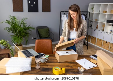 Working woman at online shop. She wearing casual clothing and checking on laptop address of customer and package information. Young woman selling products online and packaging goods for shipping.