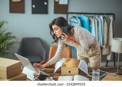 Working woman in an online store. She wears casual clothes and checks the customer's address and package information on the laptop. Online shopping concept - Shutterstock ID 2142899553