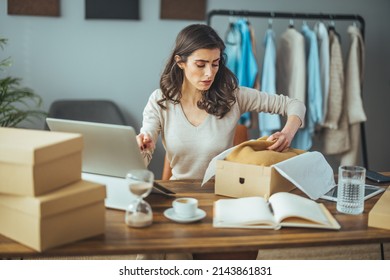 Working Woman In An Online Store. She Wears Casual Clothes And Checks The Customer's Address And Package Information On The Laptop. Online Shopping Concept