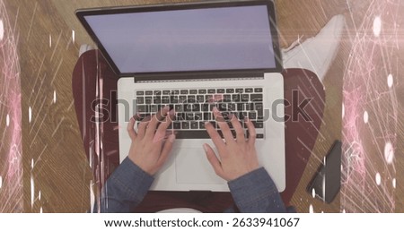 Working woman wearing denim top, burgundy pants typing on laptop on wood floor, with smartphone. Digital nomad, remote work, casual fashion, cozy environment, lifestyle, productivity, minimalist
