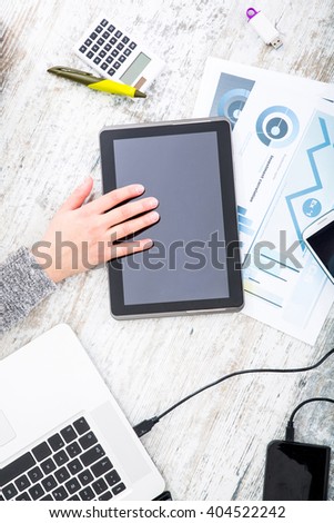 A working womans hand at a table with laptop,tablet and phone.
