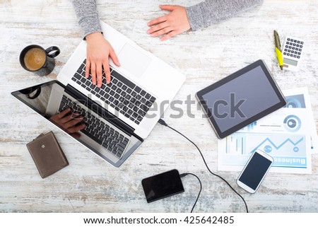 A working womans hand at a table with laptop,tablet and phone.

