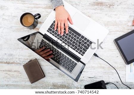 A working womans hand at a table with laptop,tablet and phone.
