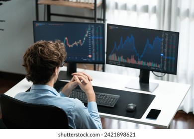 Working young business trader focusing on market stock dynamic graph data in real time two pc screens with back side at modern office. Concept of analyzing dynamic financial exchange rate. Gusher.