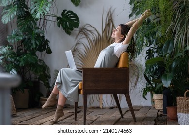 Work-life balance. Happy female freelancer with closed eyes relaxing while working remotely in home garden full of exotic plants. Young woman resting during remote work at urban jungle home office