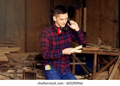 Workman Dressed In The Chekered Shirt Talking The Phone And Looking At The Sawed Wooden Blanks At The Sawmill. Timbers On Background