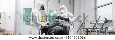 Workman in hazmat suit holding car part near colleague with polisher in service, banner