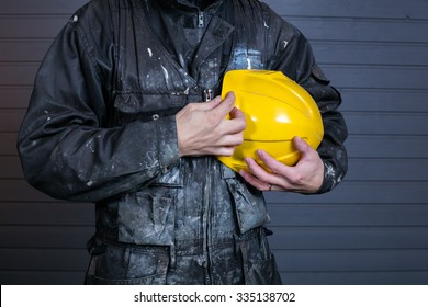 The Workman Holds In His Hand The Yellow Protective Helmet In Finland. The Overalls Are Dirty. 