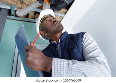 workman looking at ventilation system and making notes on clipboard