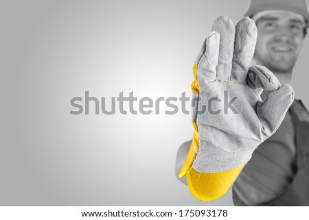 Workman making a perfect gesture with his gloved hand with focus to his hand over a grey background with a highlight and copyspace.