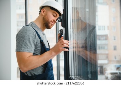 Workman in overalls installing or adjusting plastic windows in the living room at home - Shutterstock ID 2117622836
