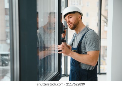 Workman in overalls installing adjusting plastic windows in the living room at home
