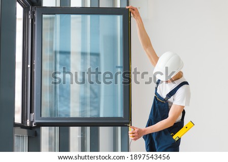 Workman in overalls installing or adjusting plastic windows in the living room at home