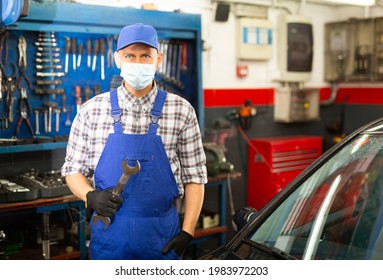 Workman In Protective Mask Standing Near Car At Auto Repair Shop