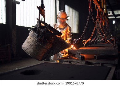 Workman in protective suit hardworking with liquid metal in foundry.