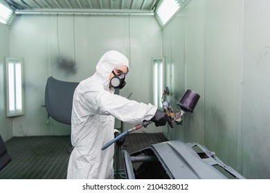 Workman In Respirator And Hazmat Suit Coloring Car Part While Working In Service