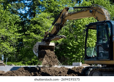 Workman using excavator, heavy construction equipment, to remove dirt to dig new house foundation, earthworks
