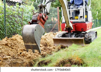 Workman using a mini digger to excavate a hole for water pipes in the garden. Czech republic, Europe.