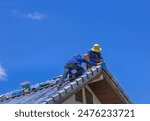 Workmans repairing leaking ridges tile roofing and replace cracked broken tile roofing on  blue  sky  background.