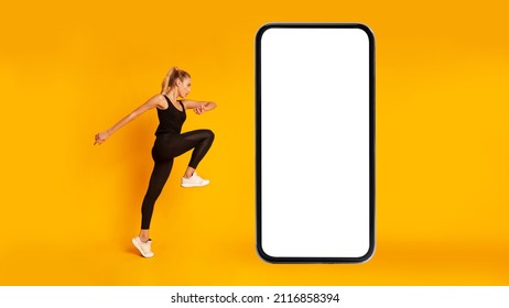 Workout Application. Fitness Woman Exercising Near Huge Phone Jumping Looking Aside In Studio Over Yellow Background. Great Mobile Offer, Gym App Concept. Panorama, Mockup