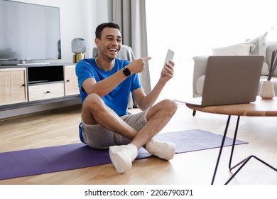 Workout Application. Happy Male Fitness Blogger Showing Smartphone To Laptop Webcam, Recommending App For Training. Online Technology, Sport Gadgets