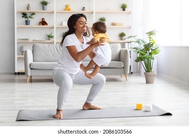 Workout With Baby. Cheerful Black Woman Exercising At Home With Infant Son, Sporty African American Female Training On Fitness Mat, Holding Her Cute Toddler Child And Making Squats, Copy Space