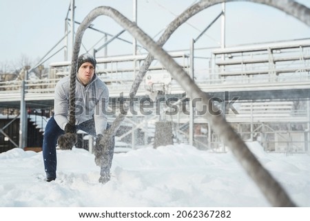 Workout with a battle ropes. Young athlete during his outdoor training during snowy winter day.