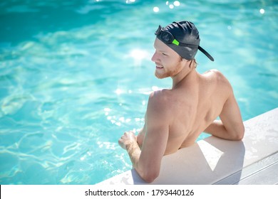 Workout Break. Smiling Male Swimmer In Black Swimming Cap Standing With His Back Turned His Head To Side Resting In Water In Pool