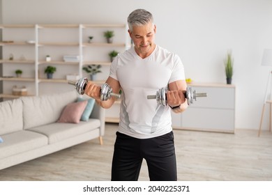 Workout During Lockdown. Athletic Middle-aged Man Doing Dumbbell Workout At Home, Looking At His Biceps, Copy Space. Mature Man Training In Living Room Interior