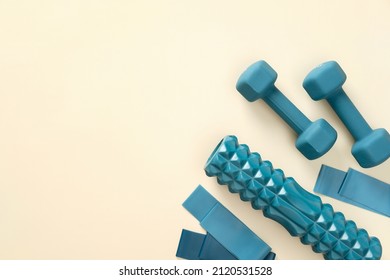 Workout equipment for training at home top view. Flat lay blue  dumbbells, elastic bands, exercise roller on beige background - Shutterstock ID 2120531528