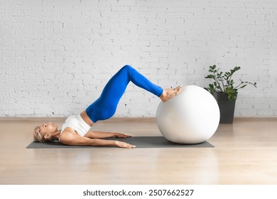 Workout with fitness ball. Fit Caucasian woman practice hamstring roll-in using props in loft studio indoor. - Powered by Shutterstock