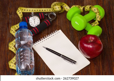 Workout and fitness dieting copy space diary. Healthy lifestyle concept. Apple, dumbbell, water, expander hand, stopwatch and measuring tape on rustic wooden table.