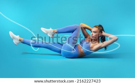 Workout. Fitness Female Flexing Abs Doing Elbow To Knee Crunch Exercising Lying On Floor Training In Studio On Blue Background With Neon Light Lines. Bodybuilding Concept