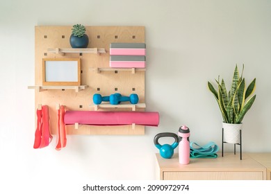 Workout fitness at home gym organized shelves for pilates equipment. Wood pegboard storing resistance bands, weights, yoga blocks, motivational message board. Women exercising at home. - Shutterstock ID 2090972974