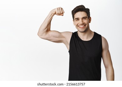 Workout and gym concept. Smiling handsome man showing his muscles after sport exercises, flexing biceps with pleased face, white background