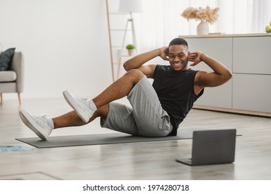 Workout. Happy Black Man Doing Elbow-To-Knee Abs Crunches Exercising At Laptop Computer Watching Online Training At Home. Sporty Guy Flexing Abdominal Muscles In Living Room